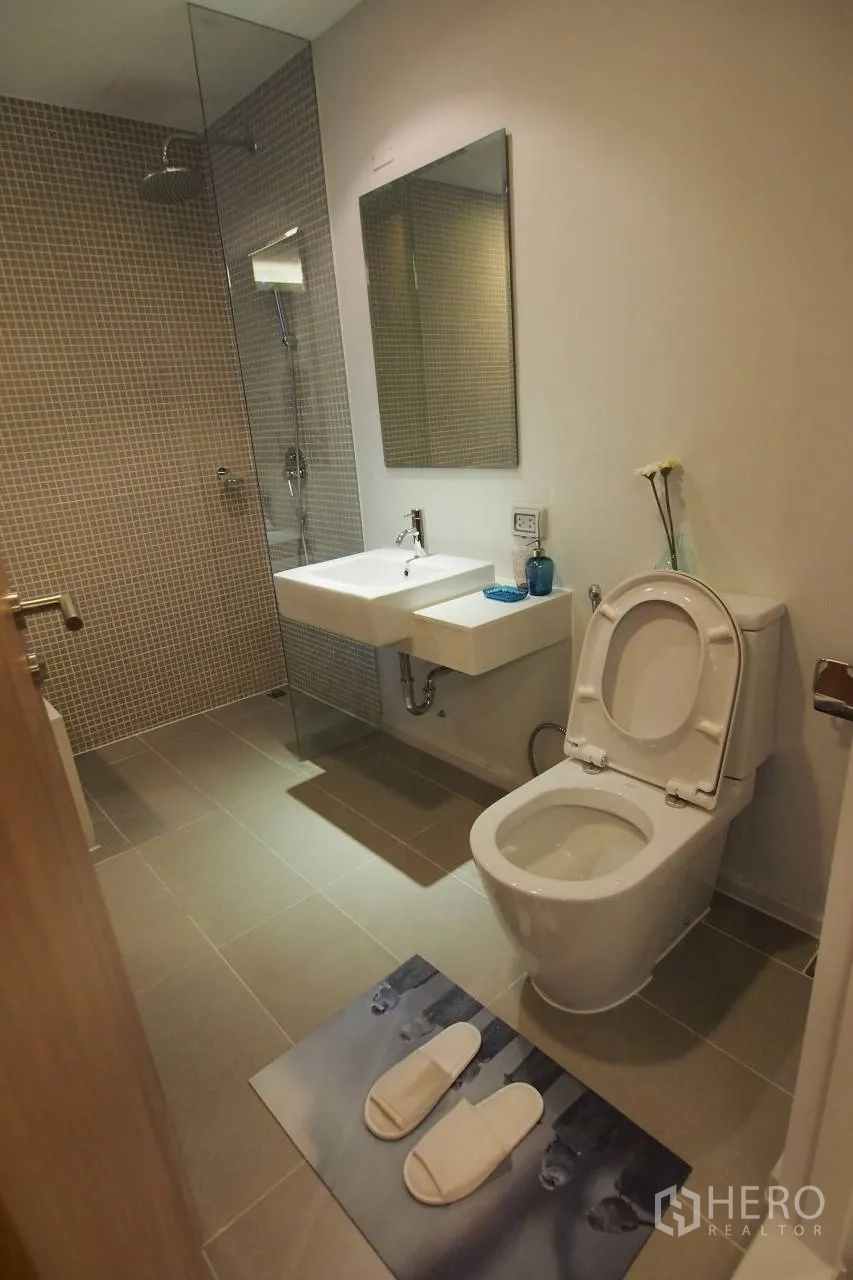 Condominium for rent in Pathum Wan, Bangkok - Contemporary bathroom with glass-enclosed rain shower, wall mirror and white sanitary ware.