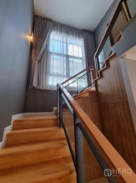 Detached House for sale in Suan Luang, Bangkok - Wood staircase with glass-and-metal railing and a tall window with sheer curtains.