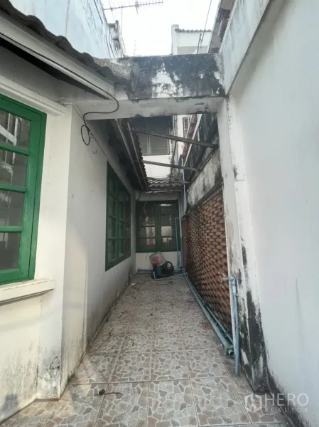 Townhouse for sale in Watthana, Bangkok - Narrow tiled side walkway with green-framed windows and exterior piping.