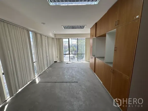 Warehouse for rent in Suan Luang, Bangkok - Bright office room with floor-to-ceiling windows, vertical blinds, and built-in wooden storage cabinets.