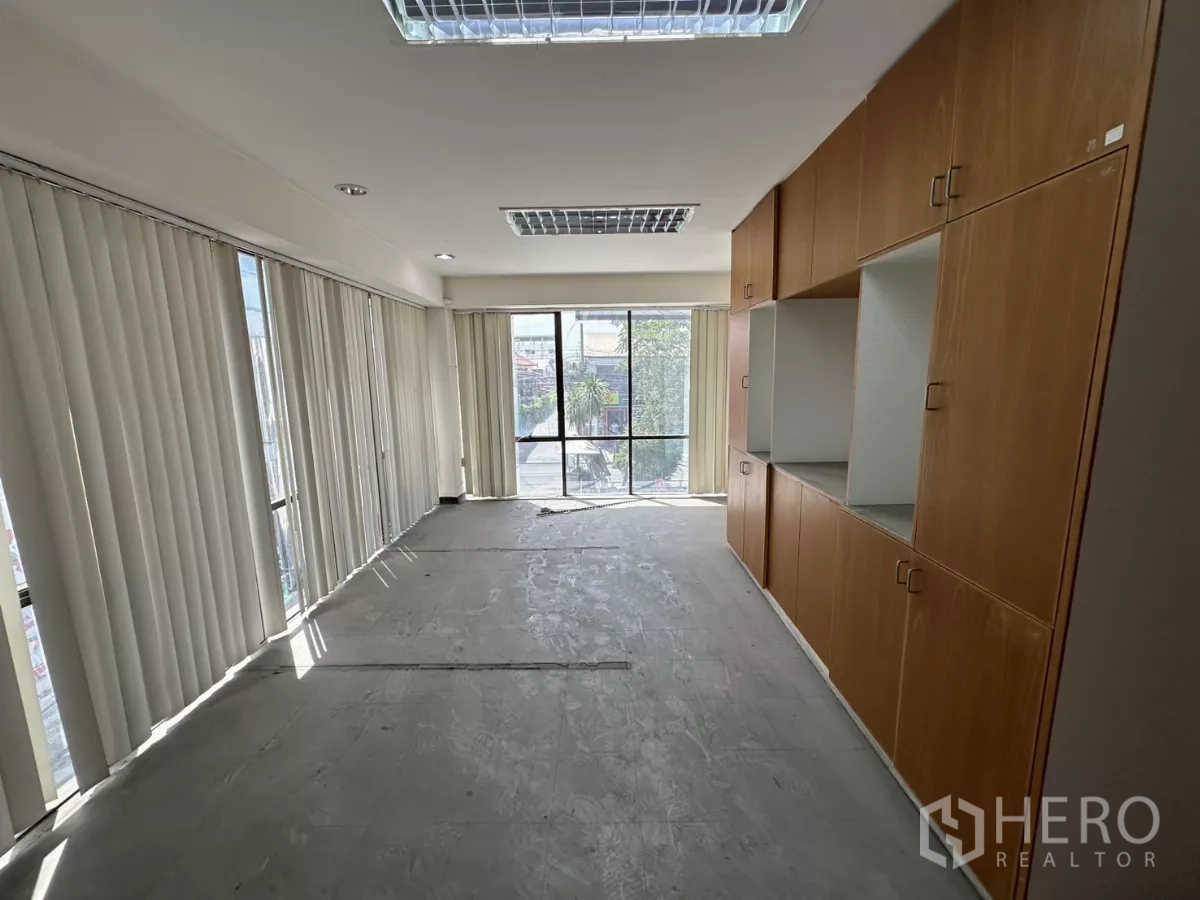 Warehouse for rent in Suan Luang, Bangkok - Bright office room with floor-to-ceiling windows, vertical blinds, and built-in wooden storage cabinets.