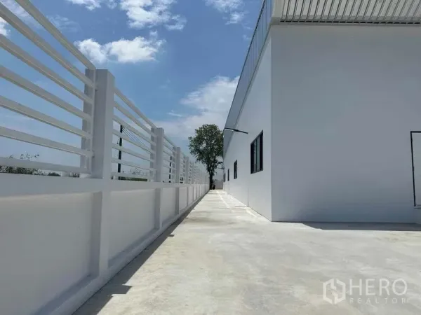 คลังสินค้า ขายในKhlong Luang, Pathum Thani - ทางเดินด้านข้างติดรั้วรอบขอบชิดสีขาวคู่ขนานกับตัวโกดัง ใต้ท้องฟ้าสีฟ้า