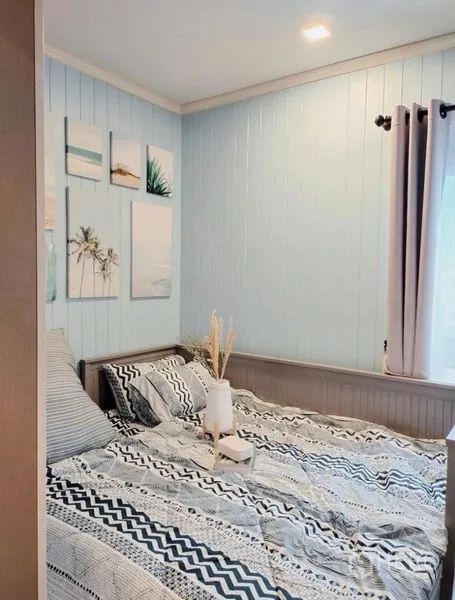 公寓 出租或出售 - 卧室以淡蓝色木质墙面与窗光营造温馨氛围，床品有图案装饰。