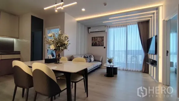 Condominium for rent in Bang Kho Laem, Bangkok - Open-plan living and dining area with LED strip lighting, TV wall and full-height windows with sheer curtains.