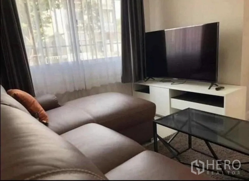 สำนักงานที่บ้าน ให้เช่าในSamut Prakan - ห้องนั่งเล่นสว่าง โซฟาหนังทรง L โต๊ะกลางกระจก และชั้นวางทีวีข้างหน้าต่างพร้อมผ้าม่าน