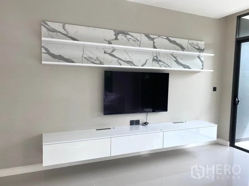 独立式住宅 出租在Saphan Sung, Bangkok - 电视墙，挂式平板电视、大理石纹置物架和白色悬空柜，旁有推拉门。
