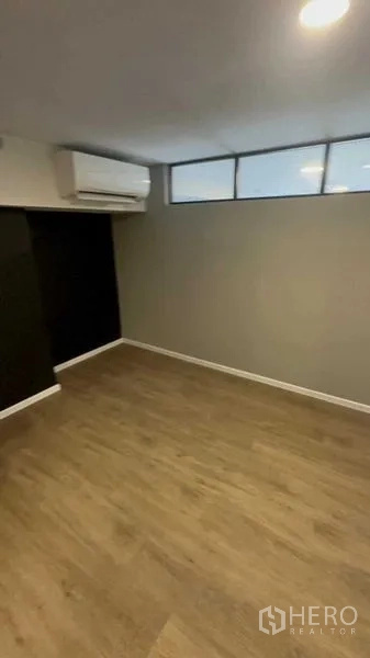Condominium for sale in Huai Khwang, Bangkok - Empty bedroom with wood floors, air conditioner and high transom windows.