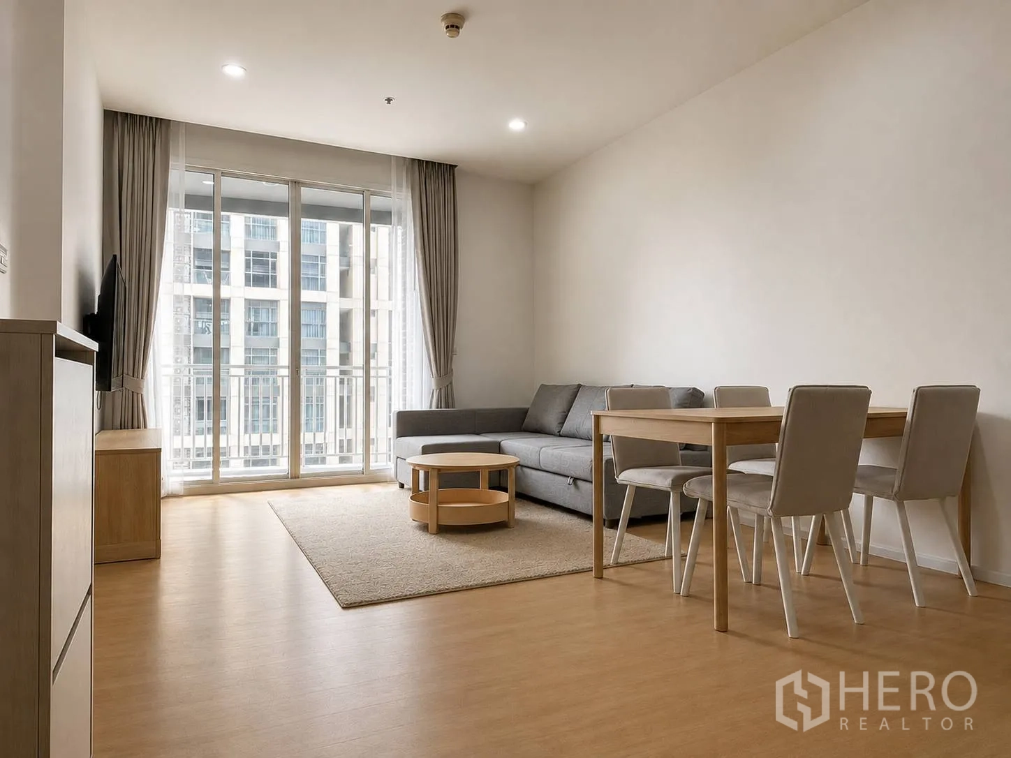 Condominium for rent or sale in Watthana, Bangkok - Living and dining area with floor-to-ceiling sliding doors to a small balcony, four-seat dining table and grey sofa.