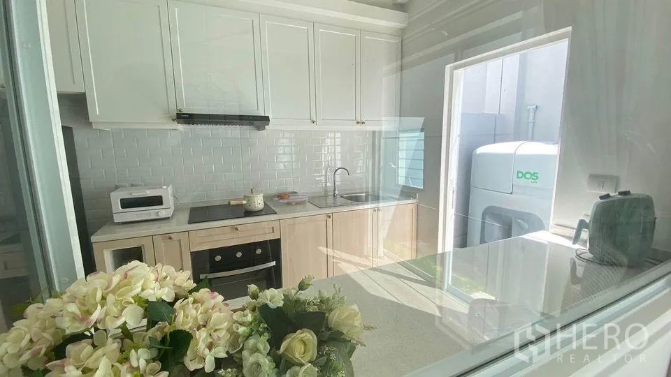 Townhouse for rent in Prawet, Bangkok - Modern closed kitchen with white cabinetry, subway-tile backsplash, built-in oven and side door to the utility area.