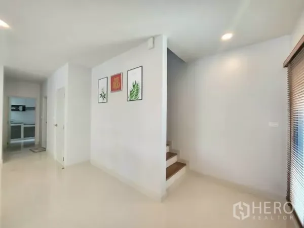 Detached House for rent in Bang Phli, Samut Prakan - Hallway with staircase and wall art leading toward the kitchen.
