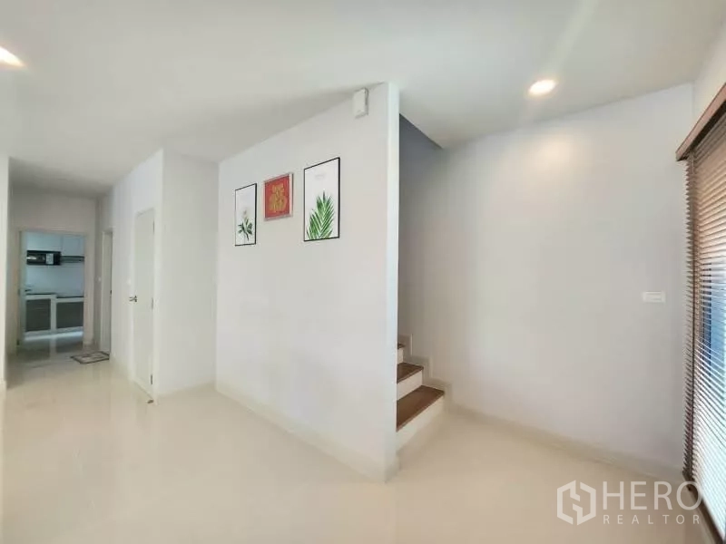 Detached House for rent in Bang Phli, Samut Prakan - Hallway with staircase and wall art leading toward the kitchen.