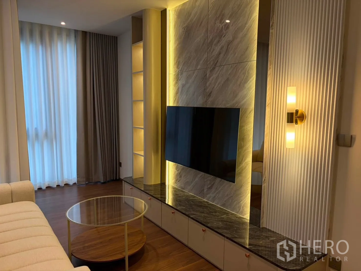 Condominium for rent in Watthana, Bangkok - Living area featuring a marble TV wall with warm backlighting and display shelves.