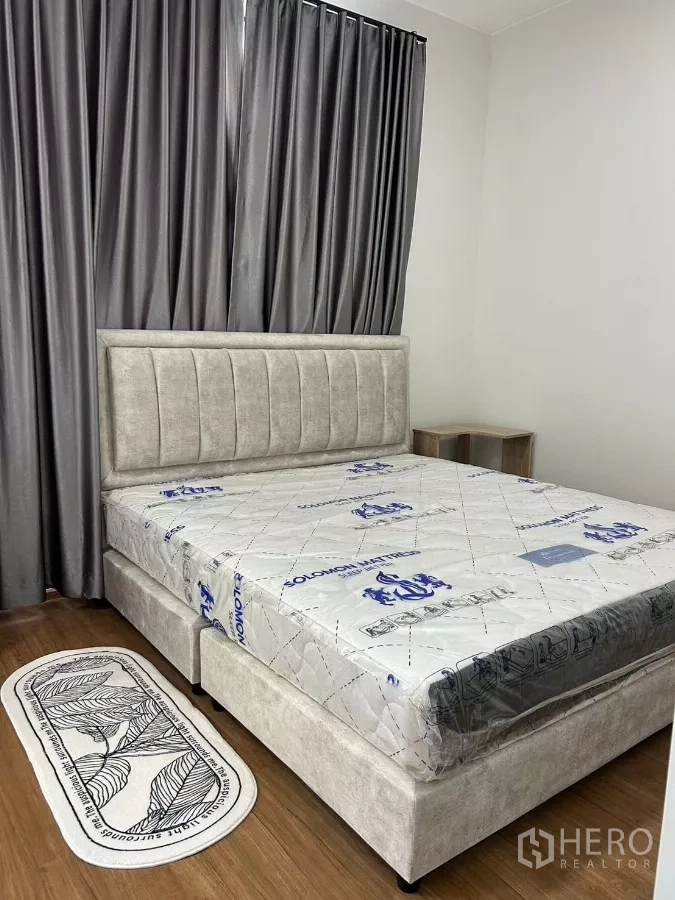 Townhouse for rent in Bang Phli, Samut Prakan - Master bedroom with upholstered bed, tall blackout curtains and wood flooring.