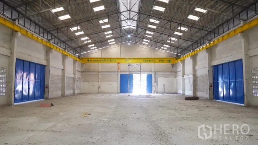 Factory for rent in Khlong Sam Wa, Bangkok - Symmetrical view of the warehouse hall with multiple blue doors and translucent roof panels.