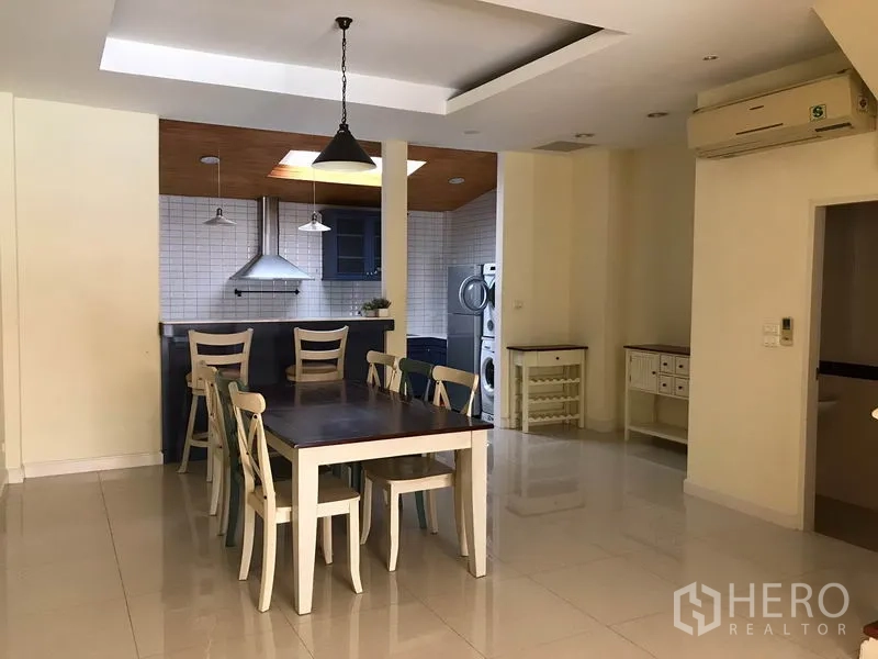 Townhouse for rent in Wang Thonglang, Bangkok - Open-plan dining area with a six-seat table and pendant lights, adjoining a tiled kitchen with skylight.