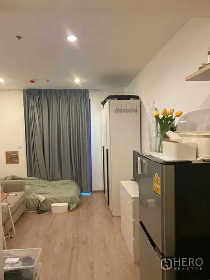 Condominium for sale in Bang Rak, Bangkok - Studio‑style layout showing bed area, gray curtains, wardrobe and kitchen appliances.
