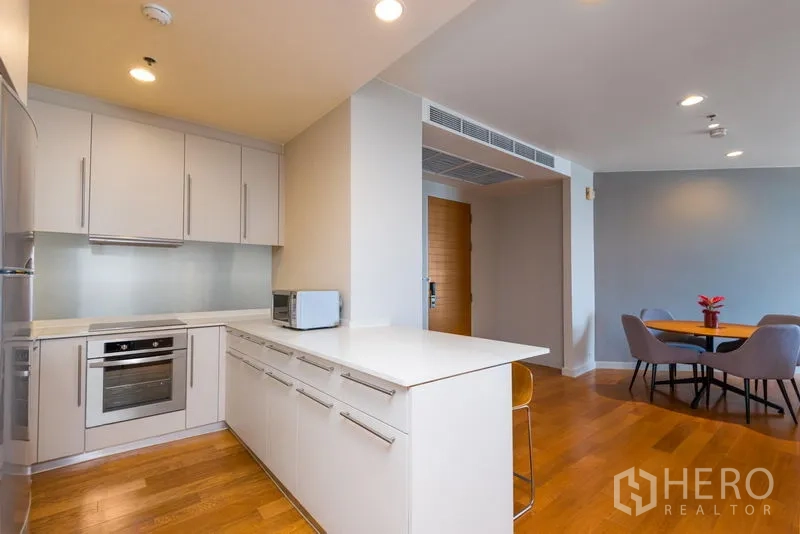 Condominium for rent in Bang Kho Laem, Bangkok - Contemporary white kitchen with built-in oven, breakfast counter and adjacent dining area.