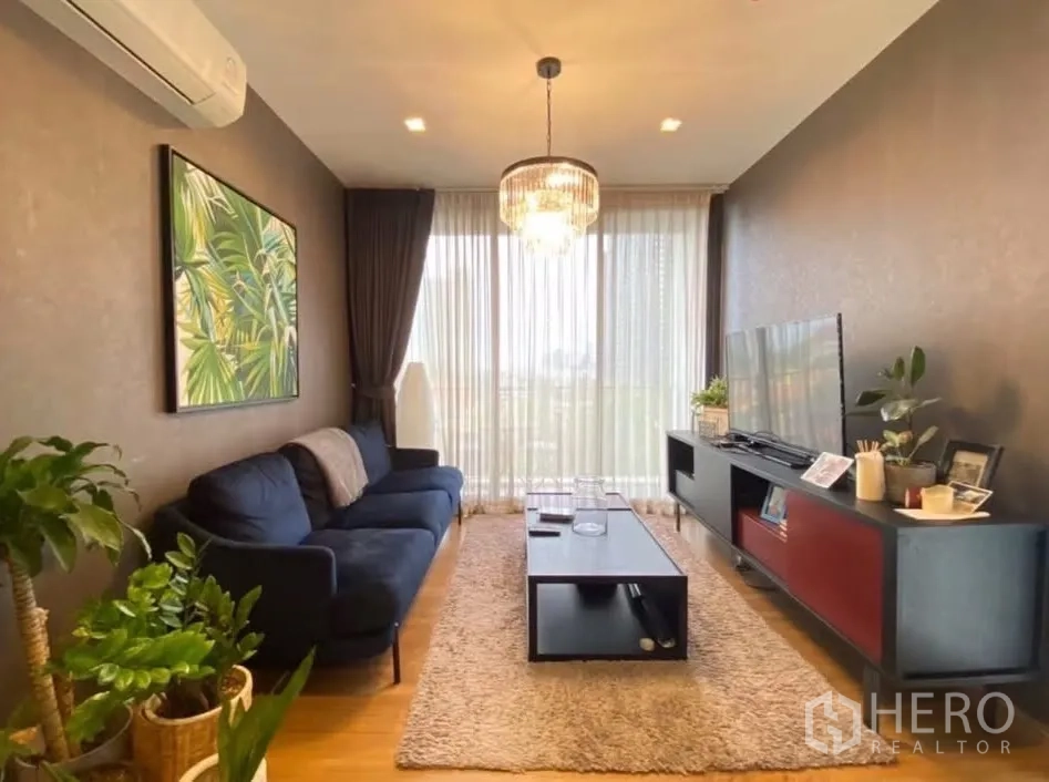 คอนโด for rent in Watthana, Bangkok - ห้องนั่งเล่นอบอุ่นด้วยโซฟาสีน้ำเงิน โคมแชนเดอเลียร์ ต้นไม้ และม่านโปร่งสูงจรดเพดาน