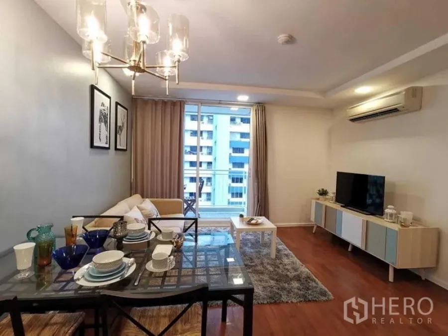 Condominium for sale in Khlong Toei, Bangkok - Living room view with dining set, chandelier, TV console, and sliding doors to balcony.