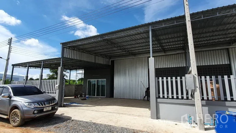 คลังสินค้า ให้เช่าในLam Luk Ka, Pathum Thani - ด้านหน้าโกดังเมทัลชีทสมัยใหม่ มีหลังคาคลุมลานโหลด รั้วเหล็ก และพื้นที่จอดรถ