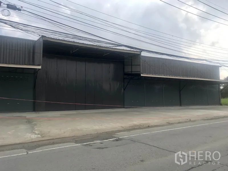 Warehouse for rent in Pathum Thani - Street-facing warehouse exterior with multiple roller shutters and wide concrete apron.