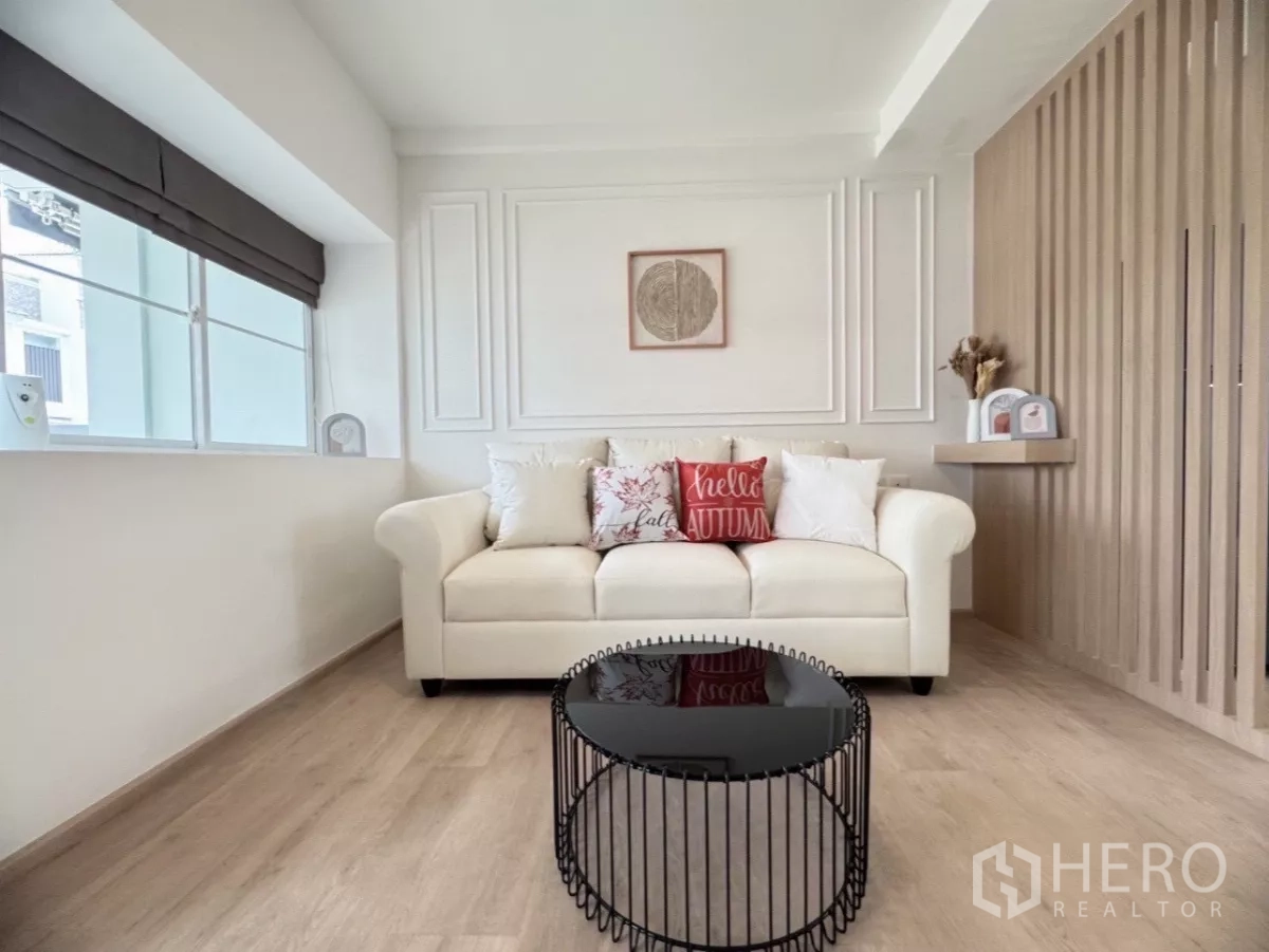 联排别墅 出租在Prawet, Bangkok - 温馨白色沙发特写，黑色圆形茶几与墙面线条装饰。