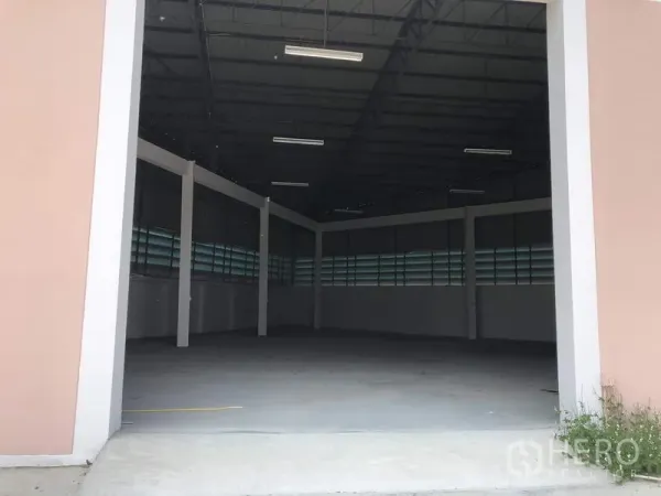 Factory for rent in Pathum Thani - Empty factory interior showing high steel roof, louvered ventilation windows, fluorescent lighting, and smooth concrete floor.