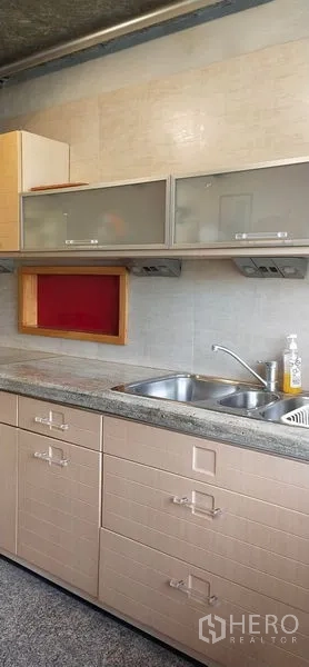公寓 出售在Watthana, Bangkok - 厨房不锈钢水槽，磨砂玻璃吊柜与浅色瓷砖墙。