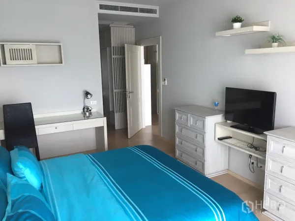 公寓 出租在Bangkok - 温馨卧室，蓝色床品，书桌、抽屉、壁架与平面电视。