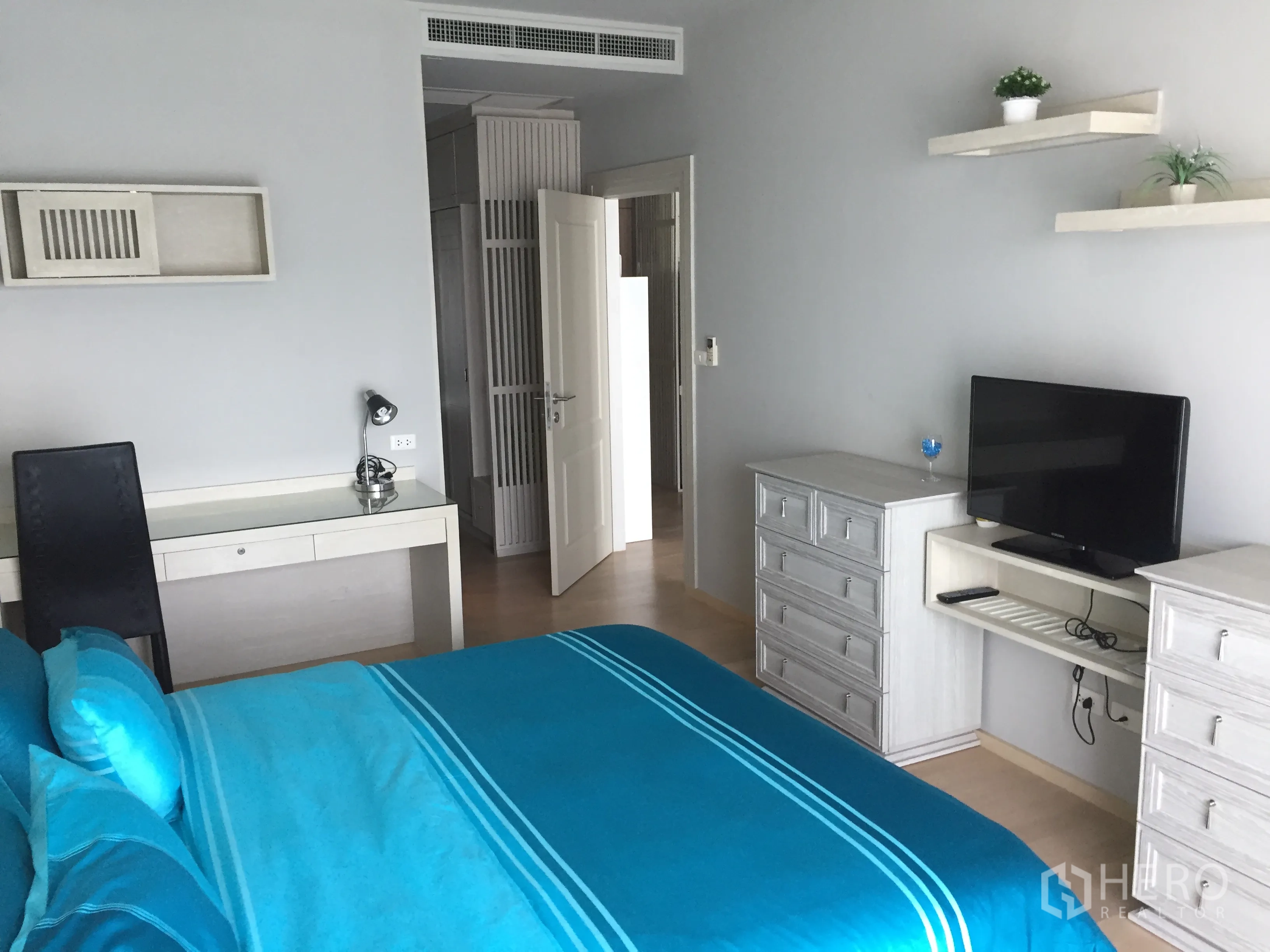 公寓 出租在Bangkok - 温馨卧室，蓝色床品，书桌、抽屉、壁架与平面电视。