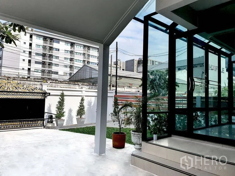 บ้าน ให้เช่าในPhra Khanong, Bangkok - เฉลียงมีหลังคา ผนังกระจก เปิดสู่สวนและทางรถ เห็นอาคารเมืองด้านนอก