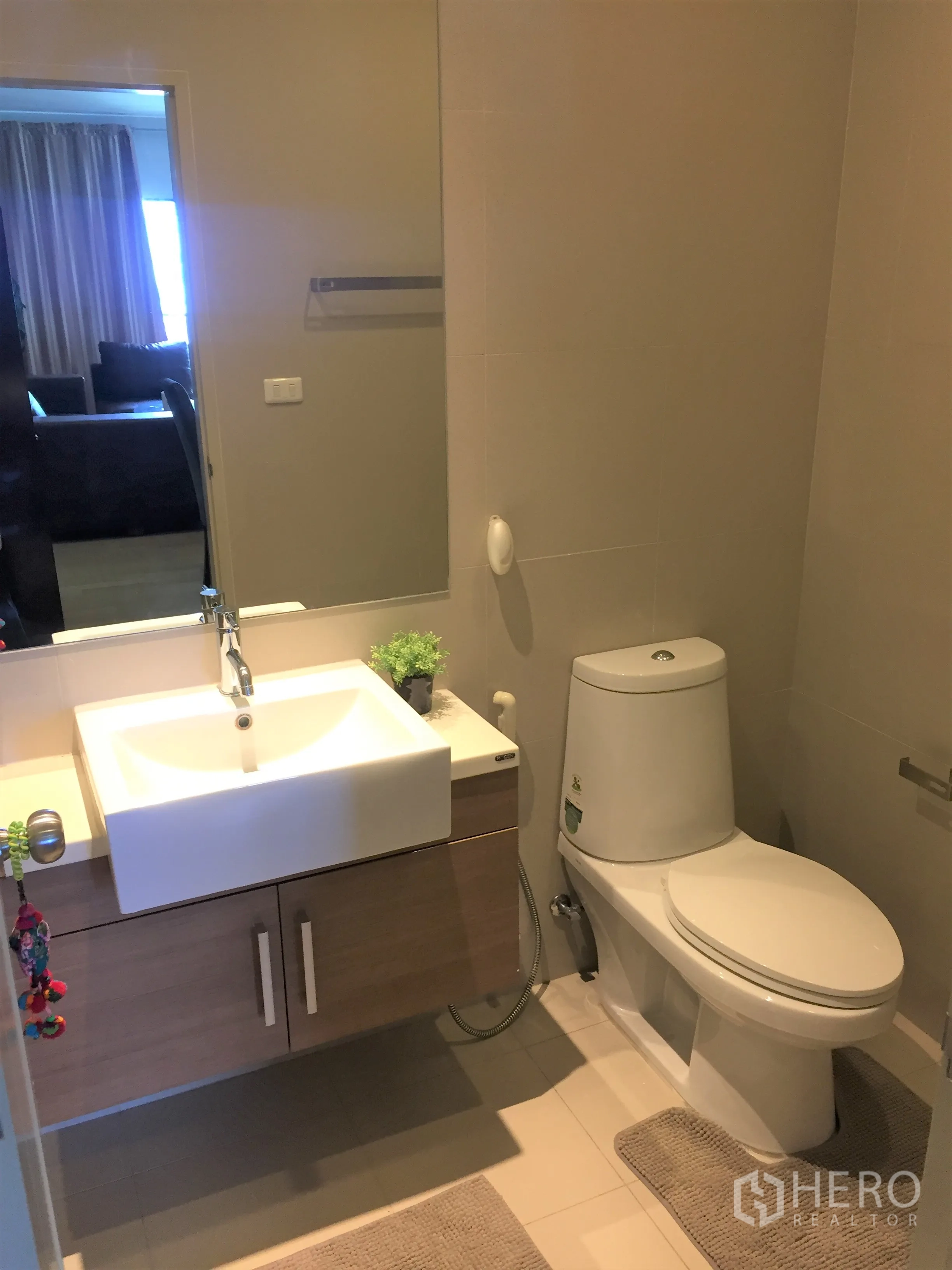Condominium for rent in Watthana, Bangkok - Contemporary bathroom featuring a floating vanity, large mirror, and toilet on neutral tiles.