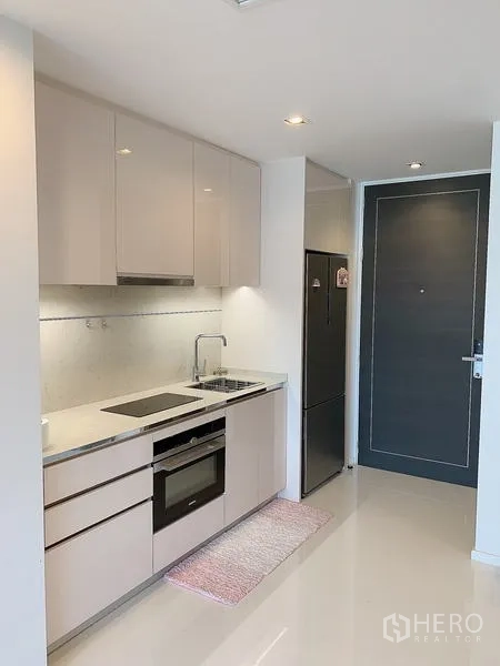 公寓 出售 - 紧凑一字型厨房，配电磁炉、烤箱与高柜冰箱。