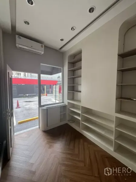 零售空间 出租在Watthana, Bangkok - 临街店铺带整面玻璃门面、空调与墙面层架，门外可停车。