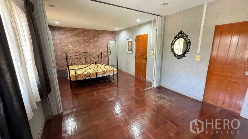 Detached House for sale in Mueang Pathum Thani, Pathum Thani - Spacious master bedroom with polished wood floors, feature wall and wrought-iron bed frame.