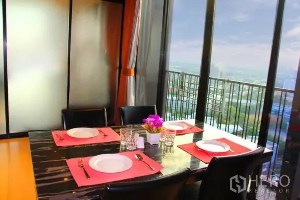 Condominium for rent or sale in Watthana, Bangkok - Dining table set beside large glass doors opening to a balcony skyline view.