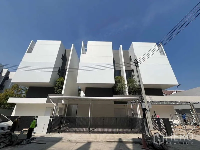 Townhouse for rent or sale in Don Mueang, Bangkok - Street-level view of the townhouse row with black fence and covered carport.