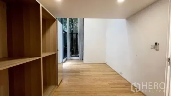 Condominium for rent in Watthana, Bangkok - Bedroom or study with built-in wooden shelving and a tall window facing a private patio.