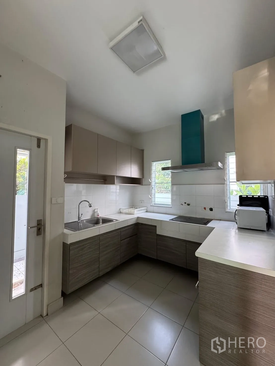 Detached House for rent in Bang Phli, Samut Prakan - L-shaped kitchen with hob, range hood, windows and ample cabinetry.