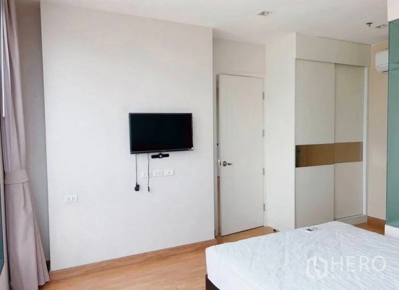 Condominium for rent in Watthana, Bangkok - Bright bedroom with wall‑mounted TV, wardrobe and light wood flooring.