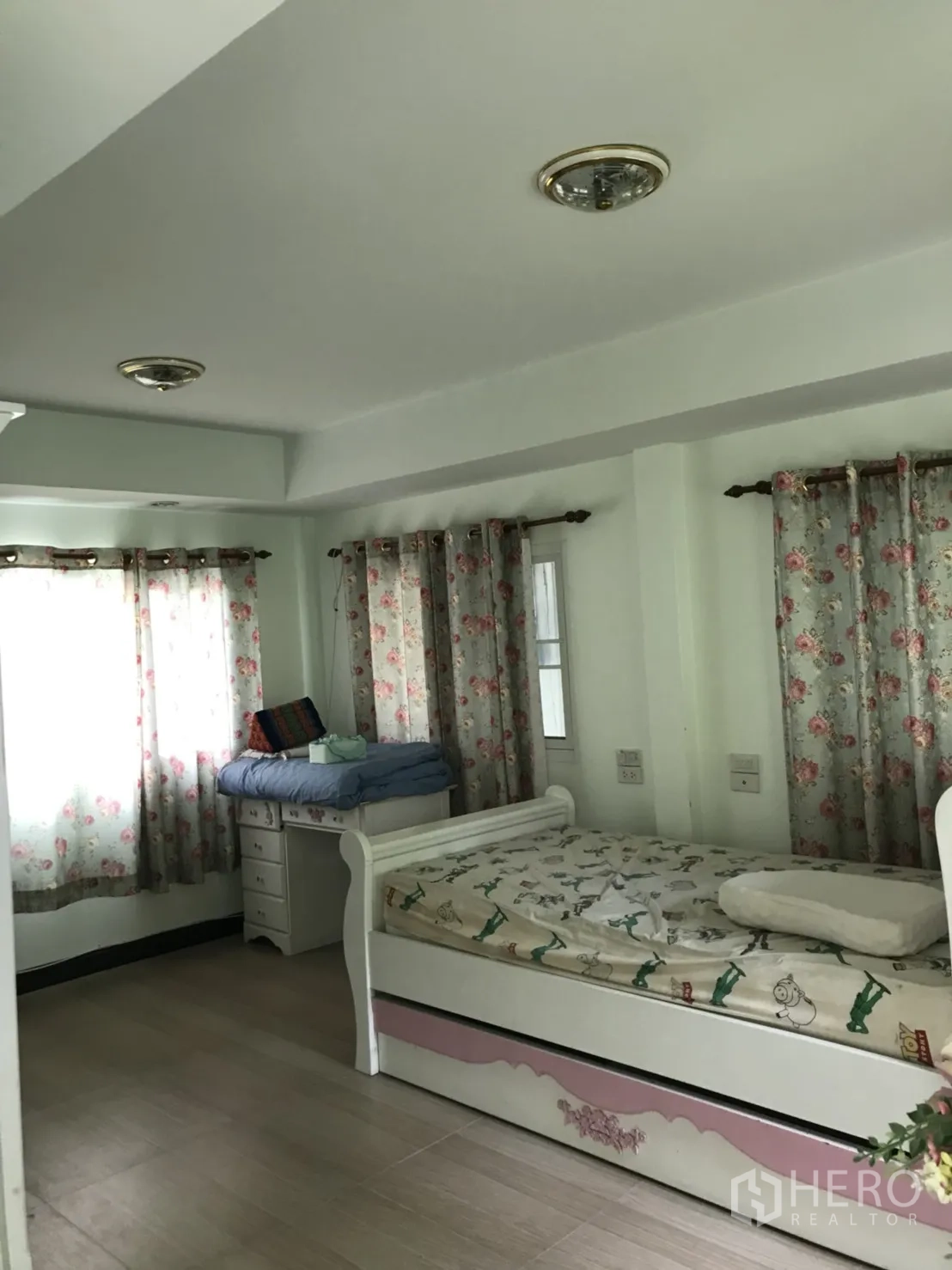 บ้าน ให้เช่าในLat Krabang, Bangkok - ห้องนอนตกแต่งพร้อม เตียงเดย์เบดสีขาว โต๊ะเขียนหนังสือ และผ้าม่านลายดอก แสงธรรมชาติเต็มห้อง