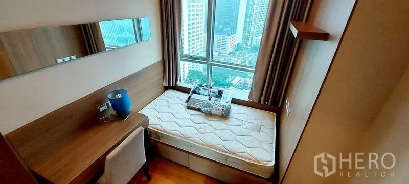 Condominium for rent in Ratchathewi, Bangkok - Cozy second bedroom with built-in desk, wood finishes, and a city-view window.