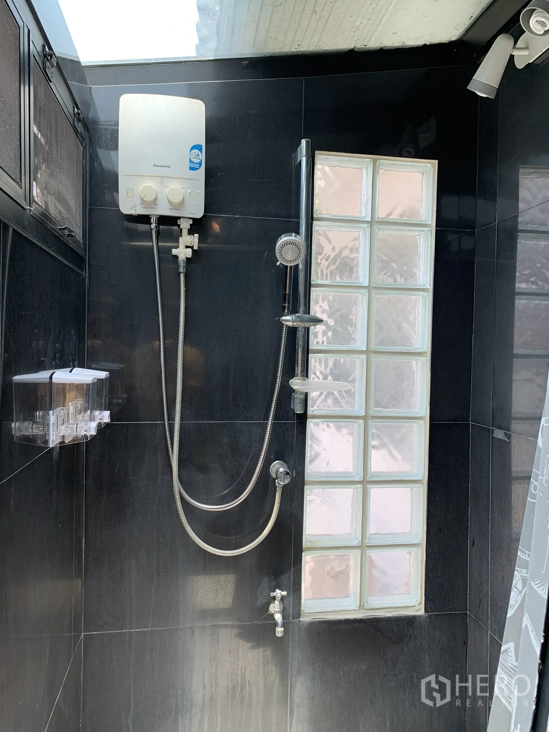 บ้านเดี่ยว for rent in Saphan Sung, Bangkok - ห้องอาบน้ำกระเบื้องสีเข้ม มีช่องกระจกบล็อก ชุดฝักบัว และเครื่องทำน้ำอุ่นใต้สกายไลท์.