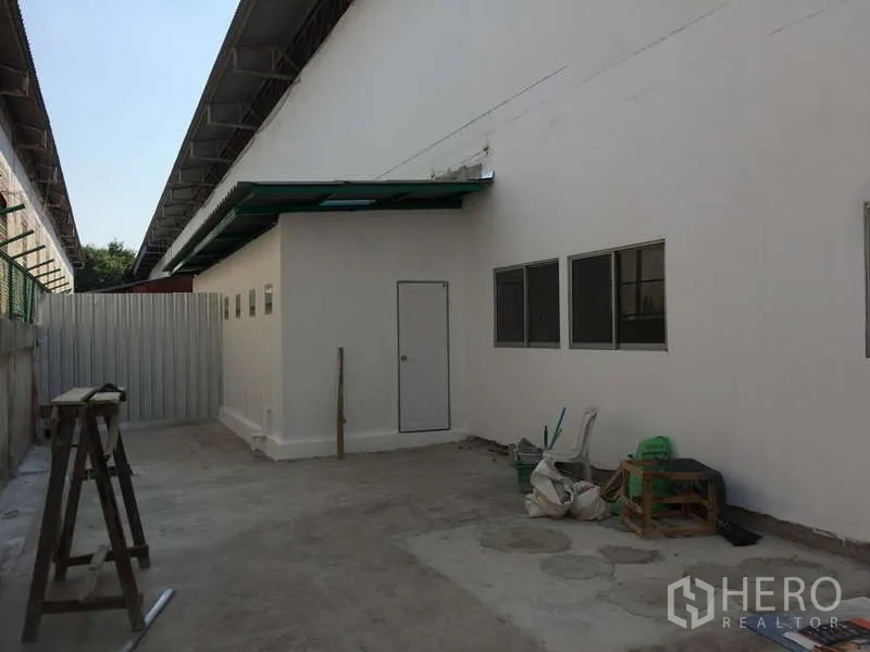 Factory for rent in Bang Bo, Samut Prakan - Rear service yard with side access door, windows and a covered walkway.