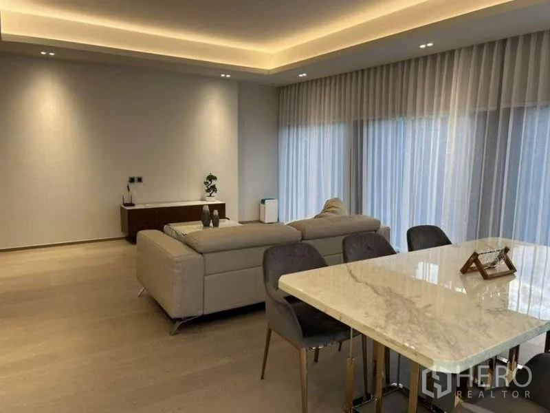 Condominium for rent in Pathum Wan, Bangkok - Open-plan living and dining with marble-top table, sofa and cove lighting.