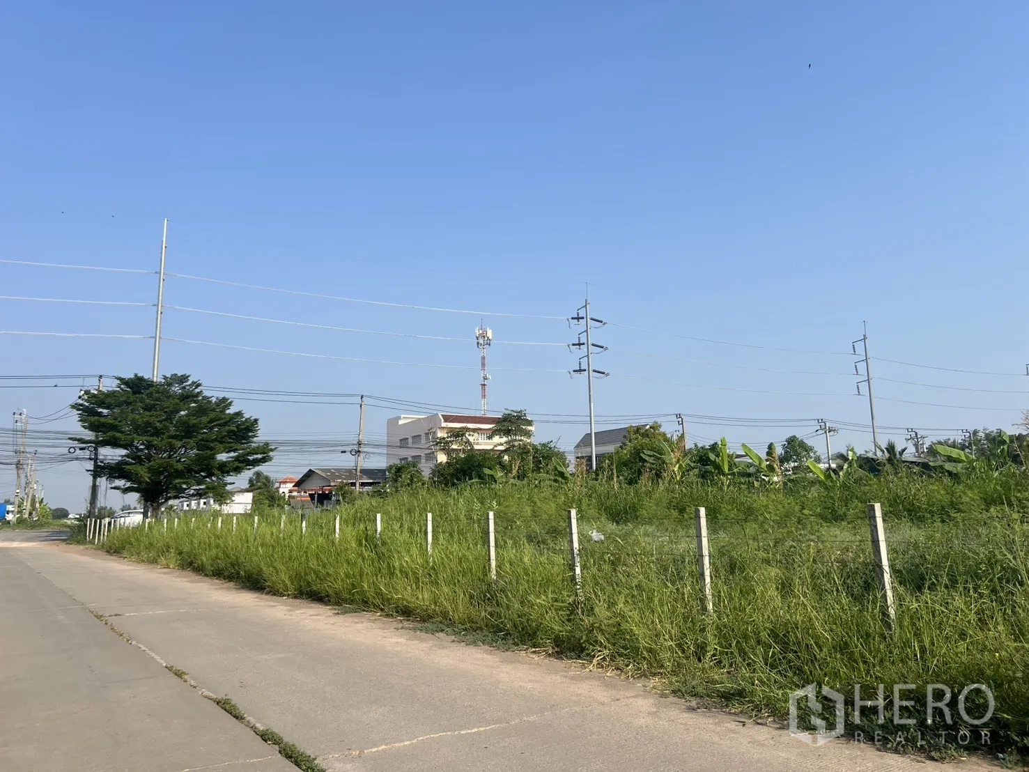 Land for sale in Lat Krabang, Bangkok - Roadside view of the land along a concrete lane with overhead cables.