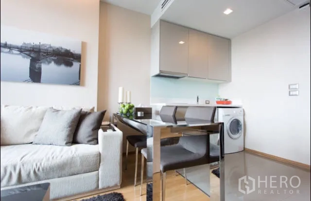 Condominium for rent in Ratchathewi, Bangkok - Compact kitchenette and dining area with glossy cabinets, glass backsplash and in-unit washing machine.
