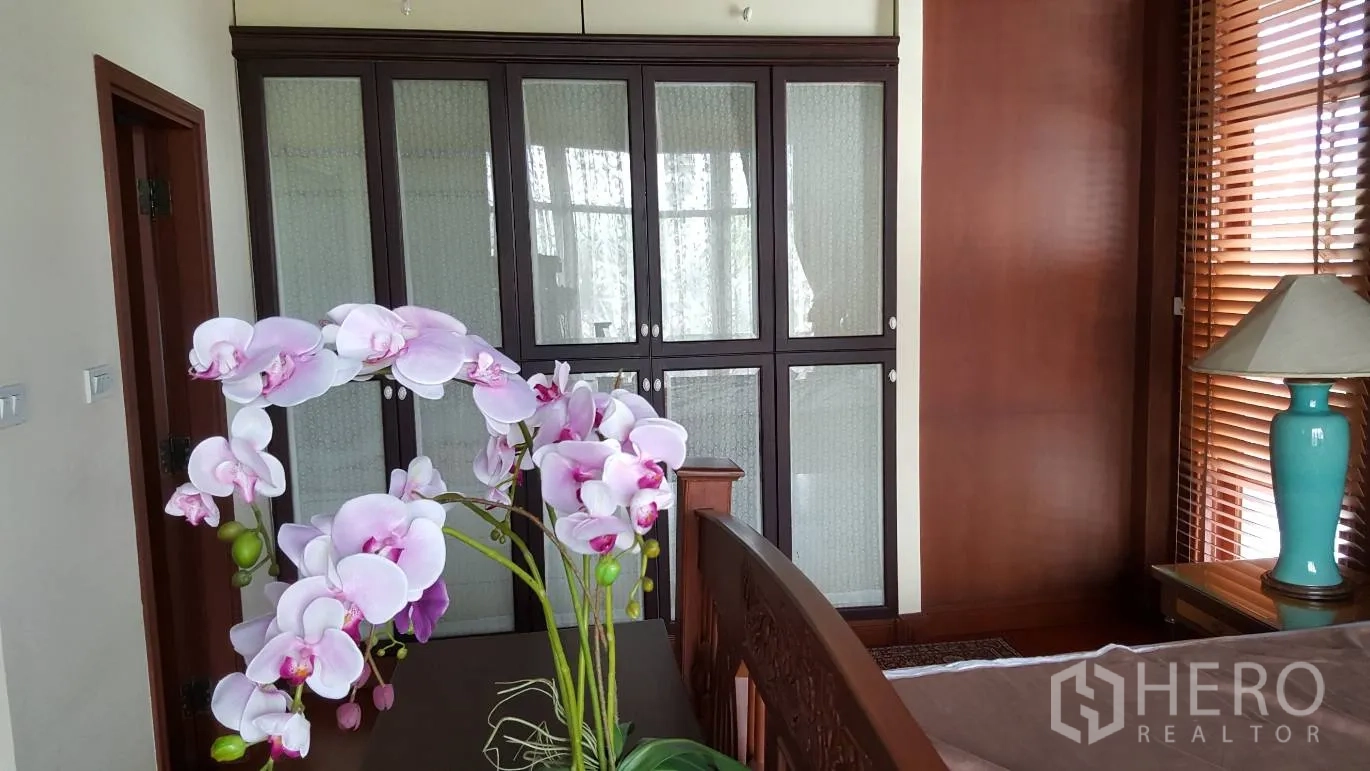 บ้าน ให้เช่าในKhlong Toei, Bangkok - ห้องนอนพร้อมตู้เสื้อผ้าบิวต์อินบานกระจก ม่านไม้ และแจกันกล้วยไม้บนโต๊ะ.