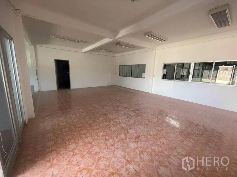 Factory for rent in Sam Khok, Pathum Thani - Open-plan admin space with terracotta tiles, ceiling lights and sliding glass door.