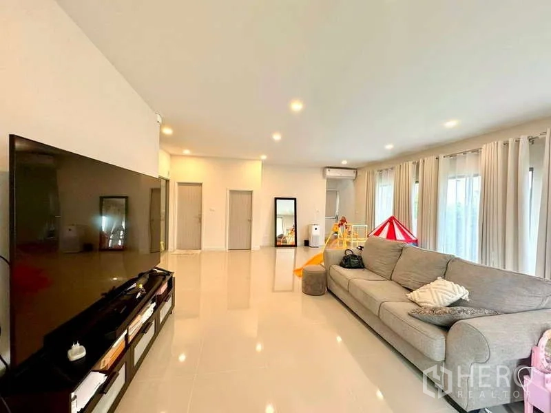 บ้าน ขายในLat Krabang, Bangkok - ห้องนั่งเล่นขนาดใหญ่ โซฟาตัวใหญ่ ผนังทีวี หน้าต่างสว่าง และไฟดาวน์ไลท์